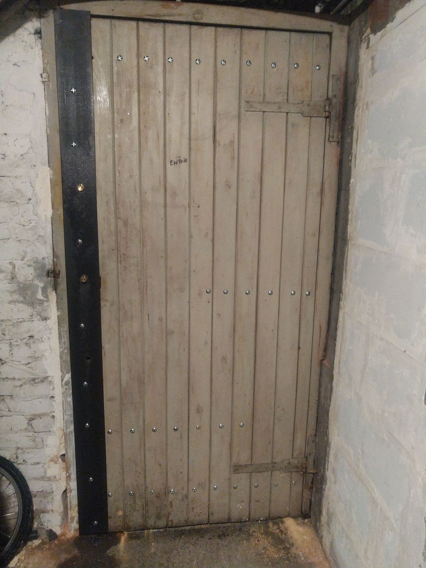 Porte étroite en bois à panneaux verticaux encastrée dans un mur de pierre brute.