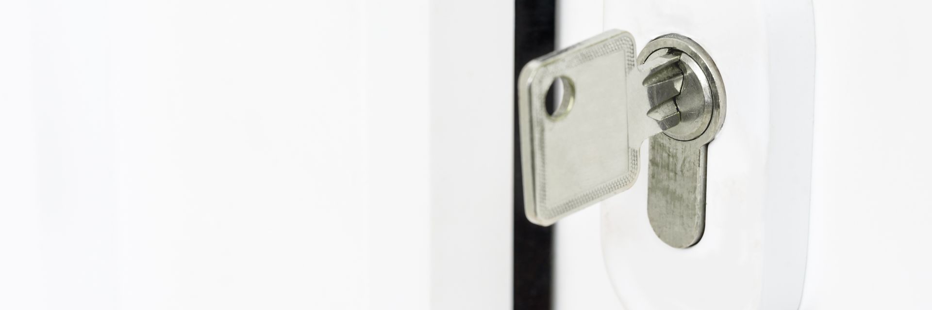 Gros plan d'une clé argentée dans une serrure sur une porte blanche