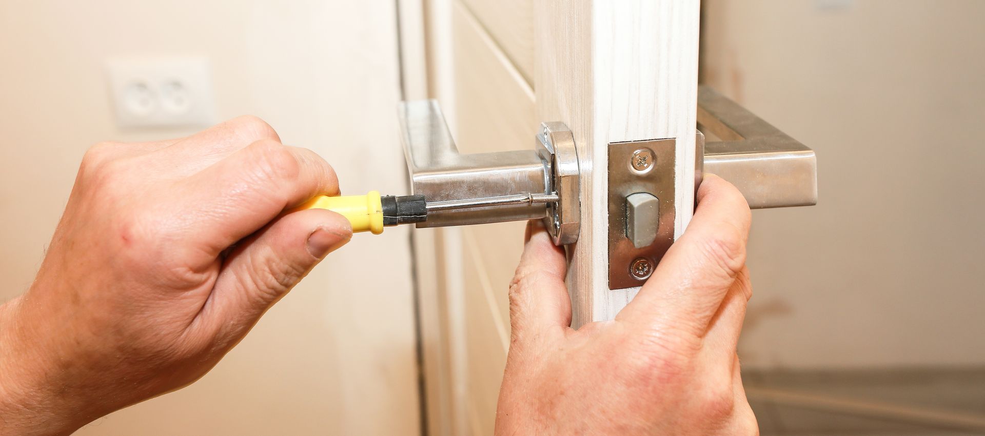Mains utilisant un tournevis pour retirer le loquet de verrouillage d'une porte intérieure blanche