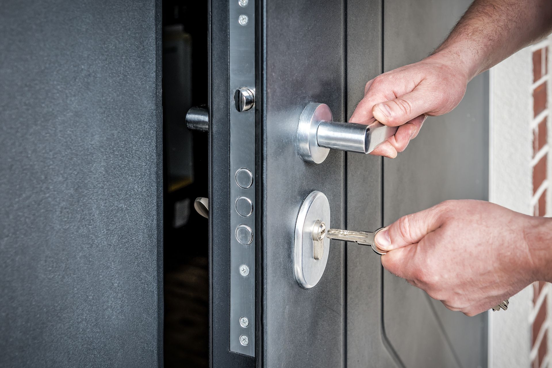 Des mains déverrouillent une porte d'entrée noire avec une clé et une poignée argentée