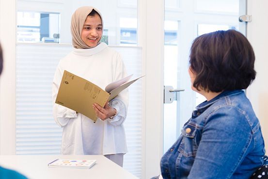 Eine Frau mit Hijab hält einen Ordner und spricht mit einer anderen Frau.