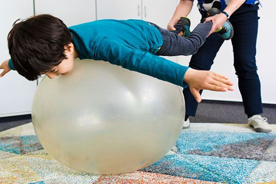 Ein kleiner Junge liegt auf einem großen Gymnastikball.