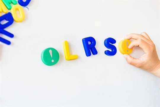 Eine Kinderhand hält die Buchstaben OLRSC auf einer weißen Tafel.