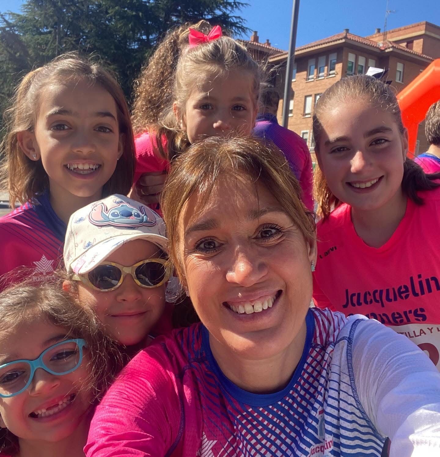 Grupo de mujeres y niñas sonrientes con camisetas rosas, posando para una selfie al aire libre.