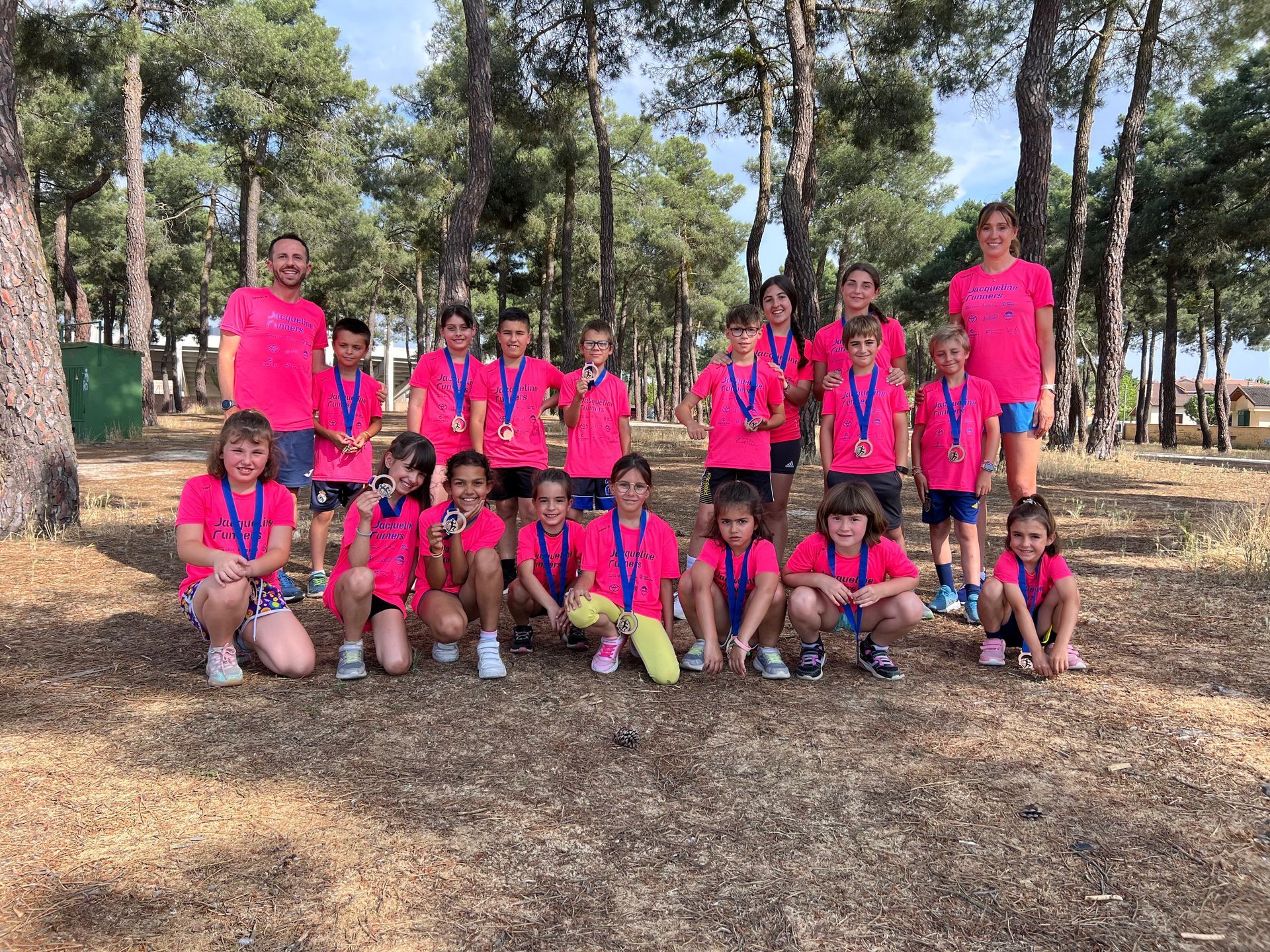 Tres jóvenes atletas de pista con uniformes rosas y azules posan en una pista azul, sonriendo.