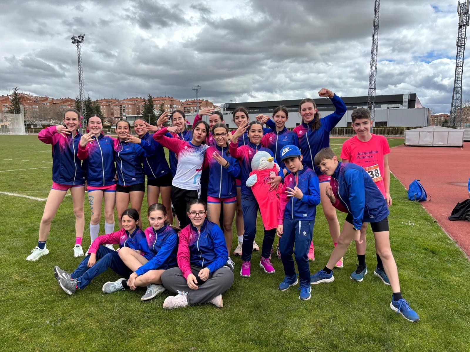 Un grupo de jóvenes atletas con chándales azules y rosas posan en un campo de césped