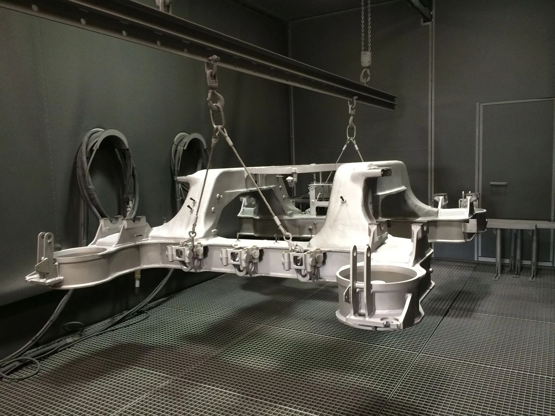 An Ketten aufgehängtes Metallchassis in einer Spritzkabine, möglicherweise zum Beschichten.