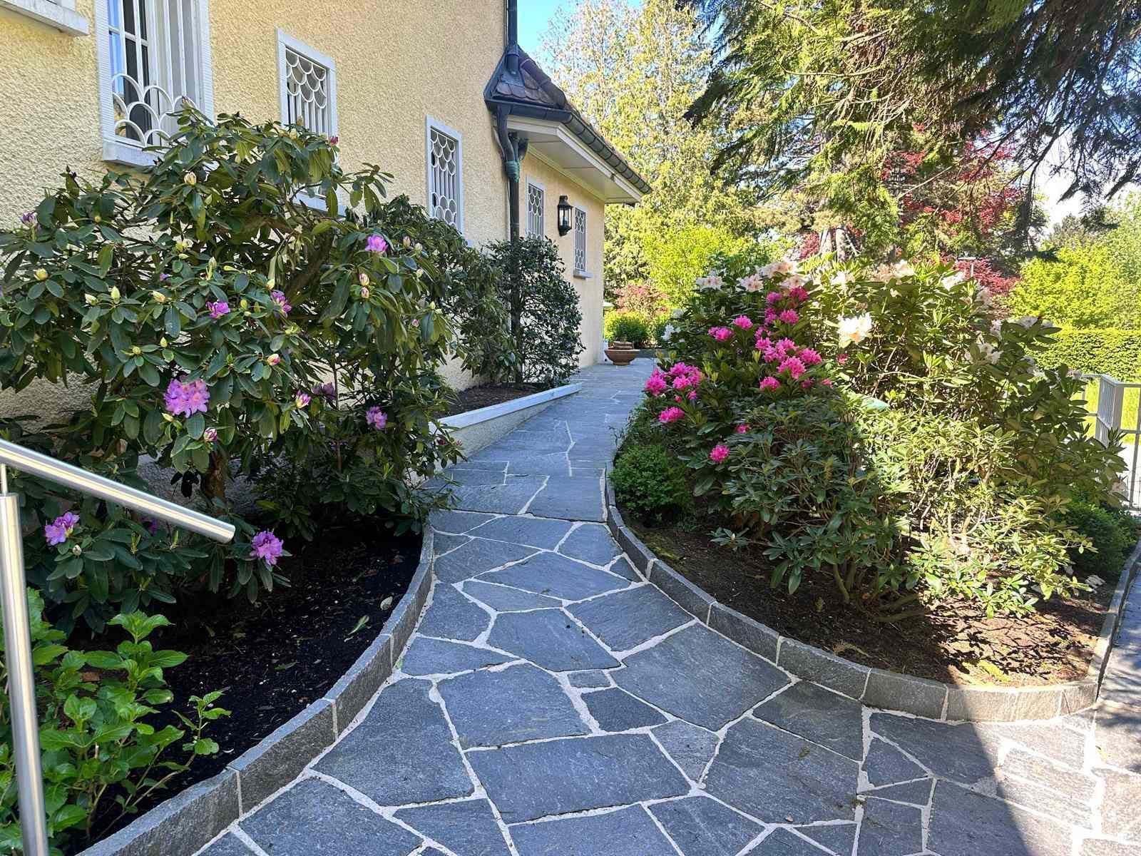 Une passerelle en pierre menant à une maison entourée de fleurs et d'arbres.