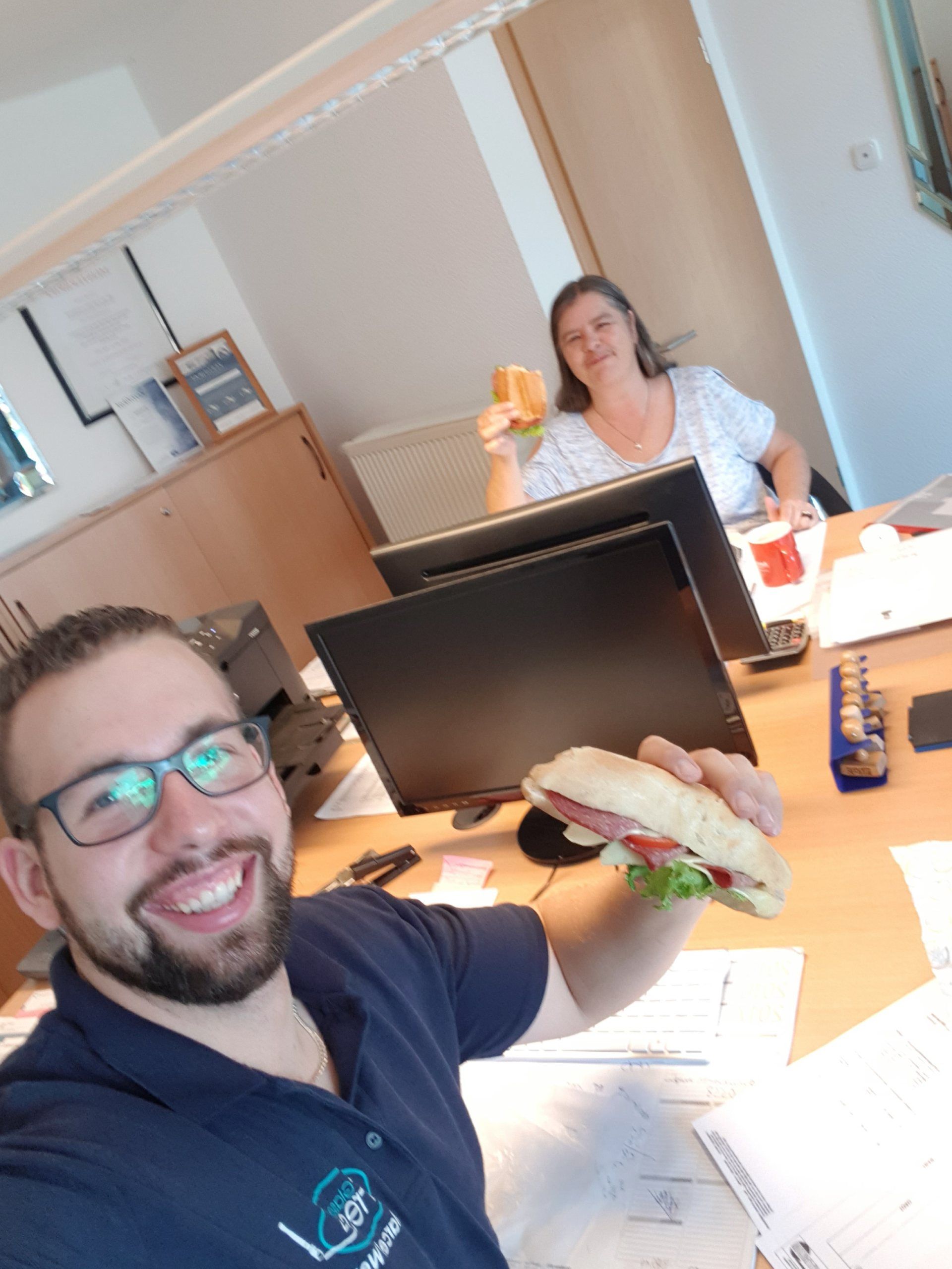 Ein Mann hält ein Sandwich vor einem Computermonitor