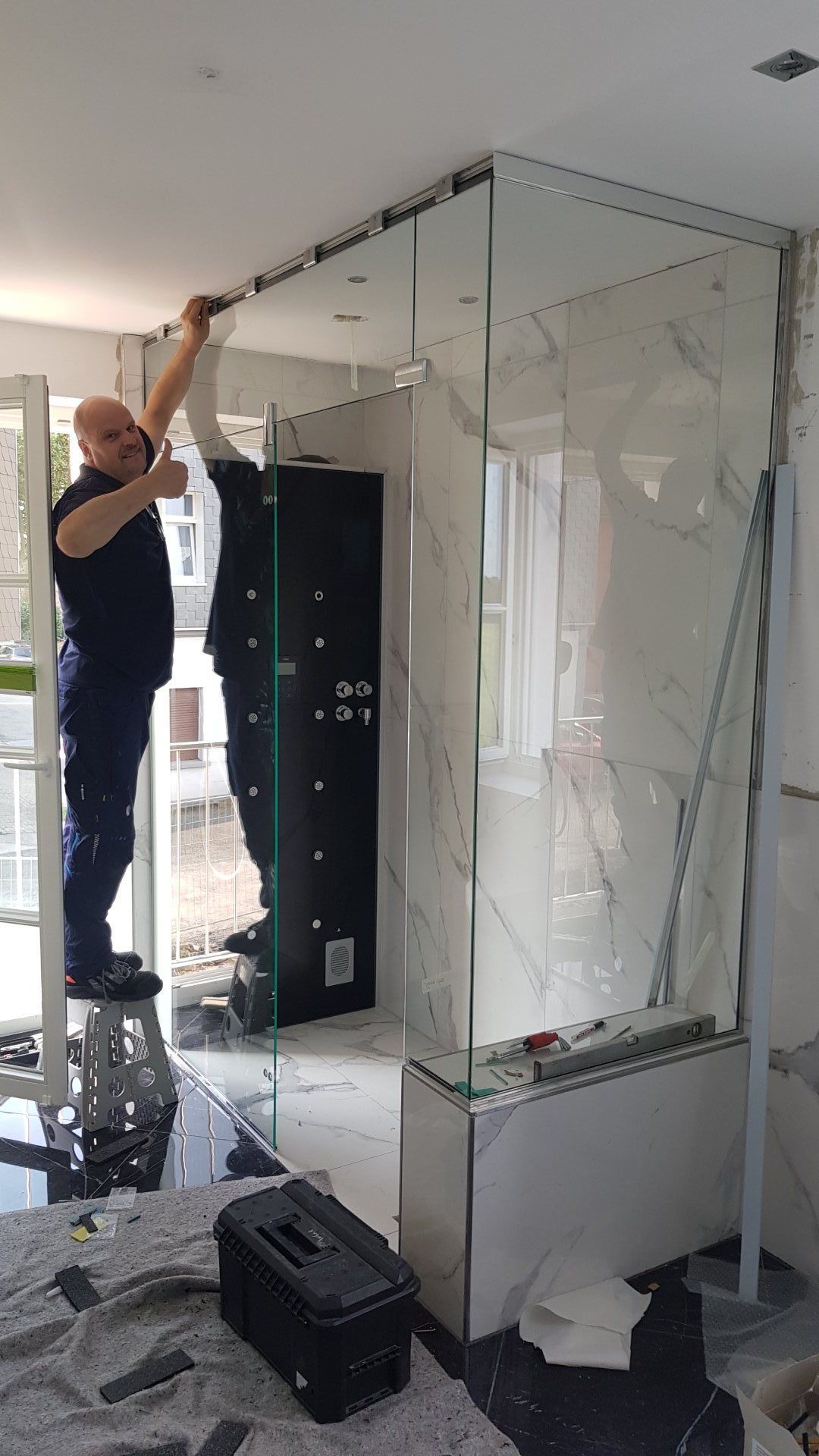 Ein Mann installiert in einem Badezimmer eine Duschtür aus Glas.