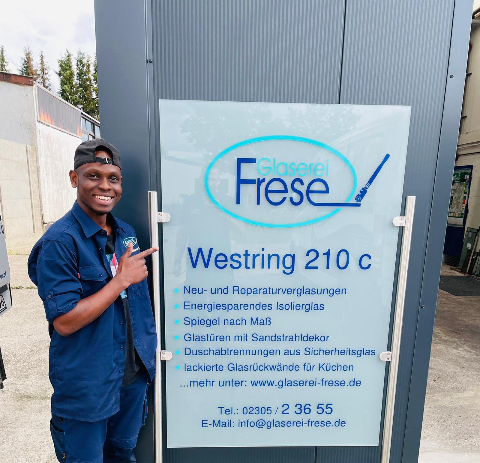 Ein Mann steht neben einem Glas-Schild mit dem Logo von Glaserei Frese