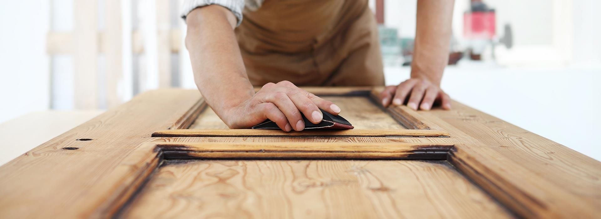 Personne ponçant un plateau de table en bois à l’aide d’une ponceuse manuelle dans un atelier lumineux