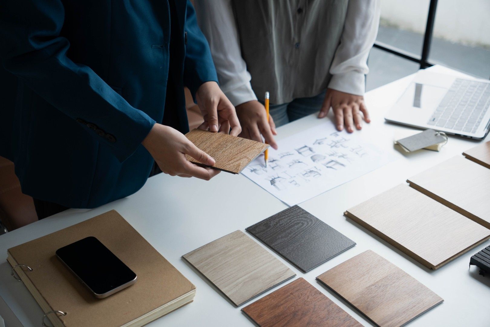 Des personnes examinent des échantillons de design et des dessins sur une table, avec des téléphones et des échantillons de tissu