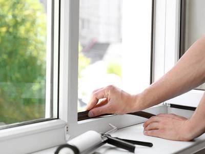 Des mains qui installent ou ajustent un store sur un rebord de fenêtre blanc, avec des outils à proximité.