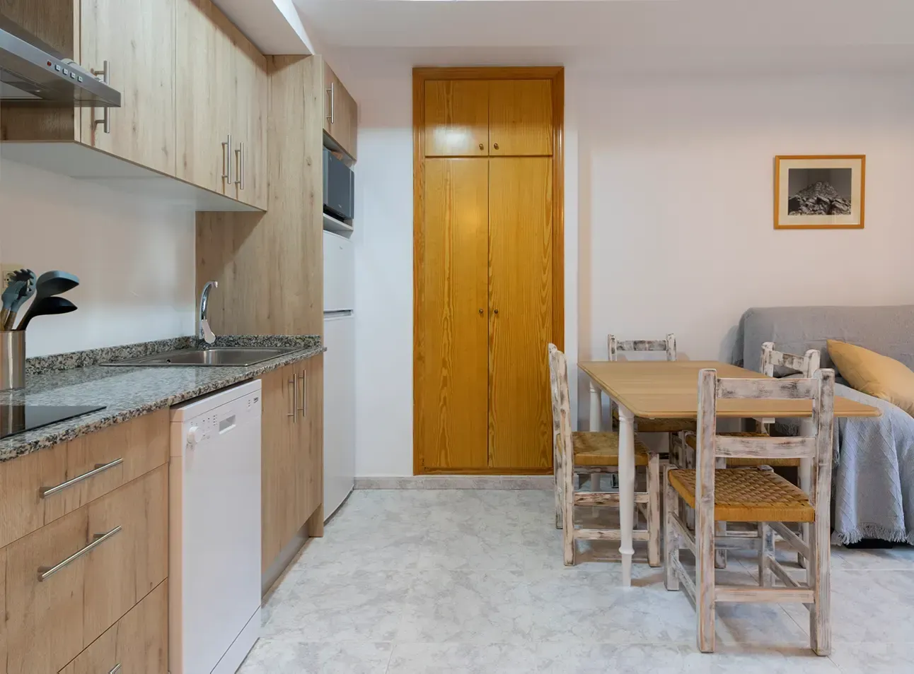 En el interior de una vivienda, se encuentra una zona de cocina con armarios de madera y encimeras de granito