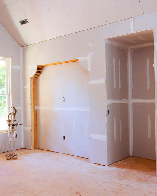 Une pièce inachevée avec des cloisons sèches, un cadre d'alcôve en bois et une porte ouverte donnant sur un placard.