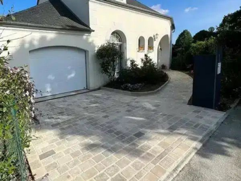 Entrée et allée en pavés beiges devant une porte de garage