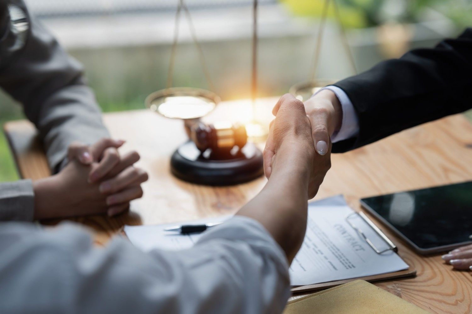 Dos personas se dan la mano al hablar de un documento legal, con el mazo del juez y la balanza de la justicia
