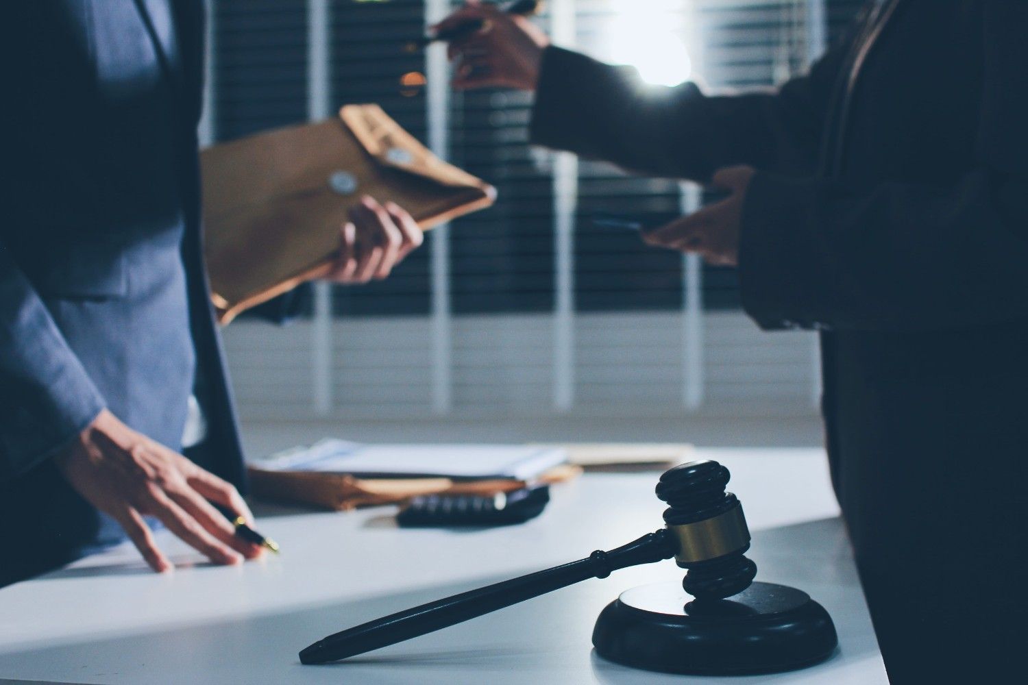 Un mazo reposa sobre una mesa frente a dos profesionales con traje, uno de ellos sosteniendo un documento