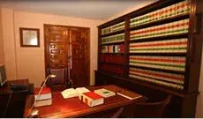 Un escritorio de madera con libros abiertos se encuentra en una oficina en casa que cuenta con grandes estanterías empotradas