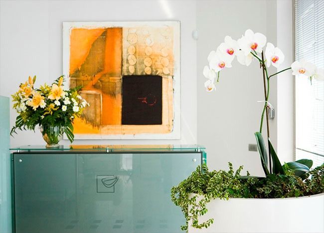 Un interior luminoso con arte abstracto, una orquídea y un arreglo floral en un armario verde azulado.