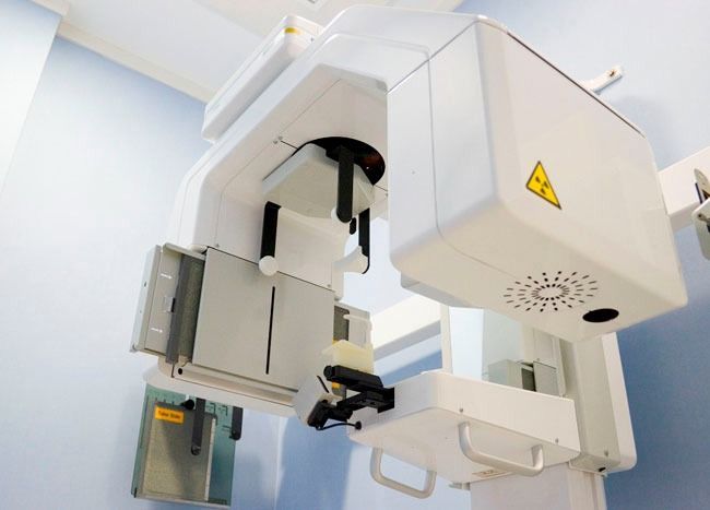 Máquina de rayos X panorámicos dentales, de color blanco, en una clínica de paredes azules.