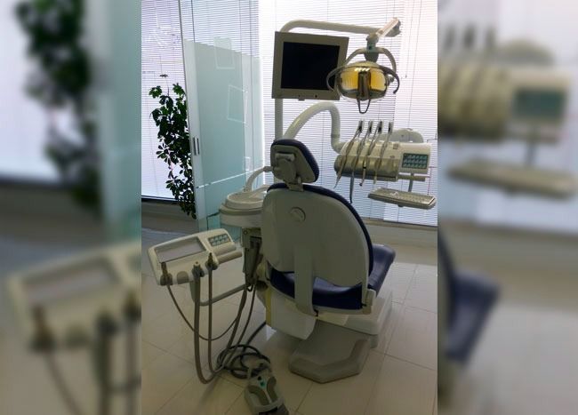 Sillón dental en entorno clínico con herramientas y monitor.
