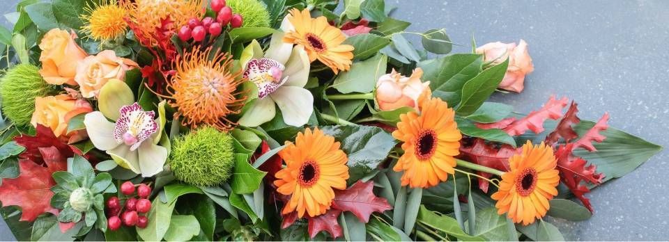 Composition de gerberas orange, d'orchidées, de fleurs vertes et de baies ; disposée sur une surface grise.