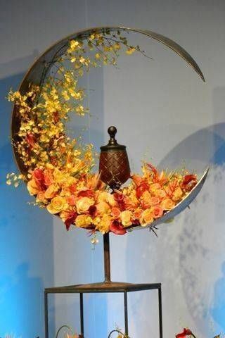 Composition florale en forme de croissant de lune avec des fleurs orange et jaunes et une lanterne.