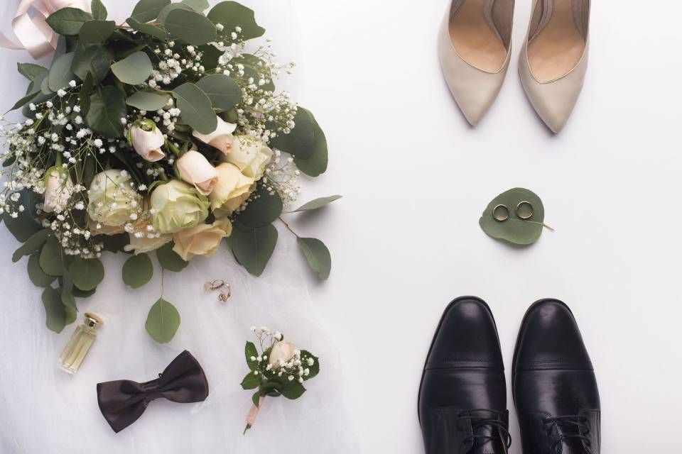 Détails du jour du mariage : bouquet, chaussures, alliances, nœud papillon, boutonnière, parfum et chaussures du marié sur fond blanc.