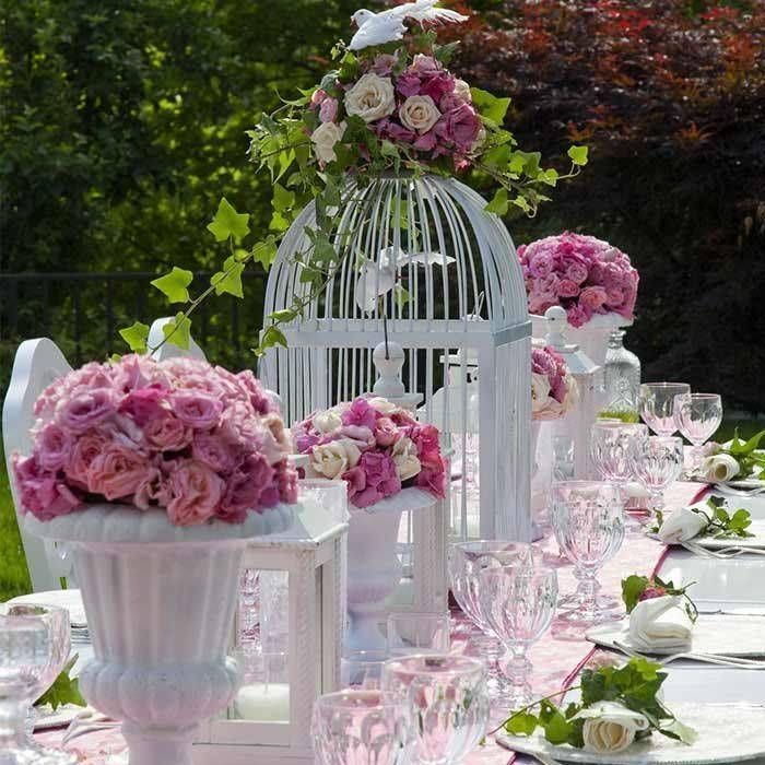 Élégante décoration de table en extérieur avec des roses roses, des touches de blanc et un centre de table en forme de cage à oiseaux.