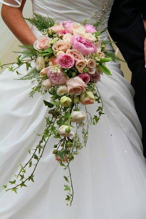 La mariée en robe blanche tient un bouquet cascade de fleurs roses et crème et de verdure.