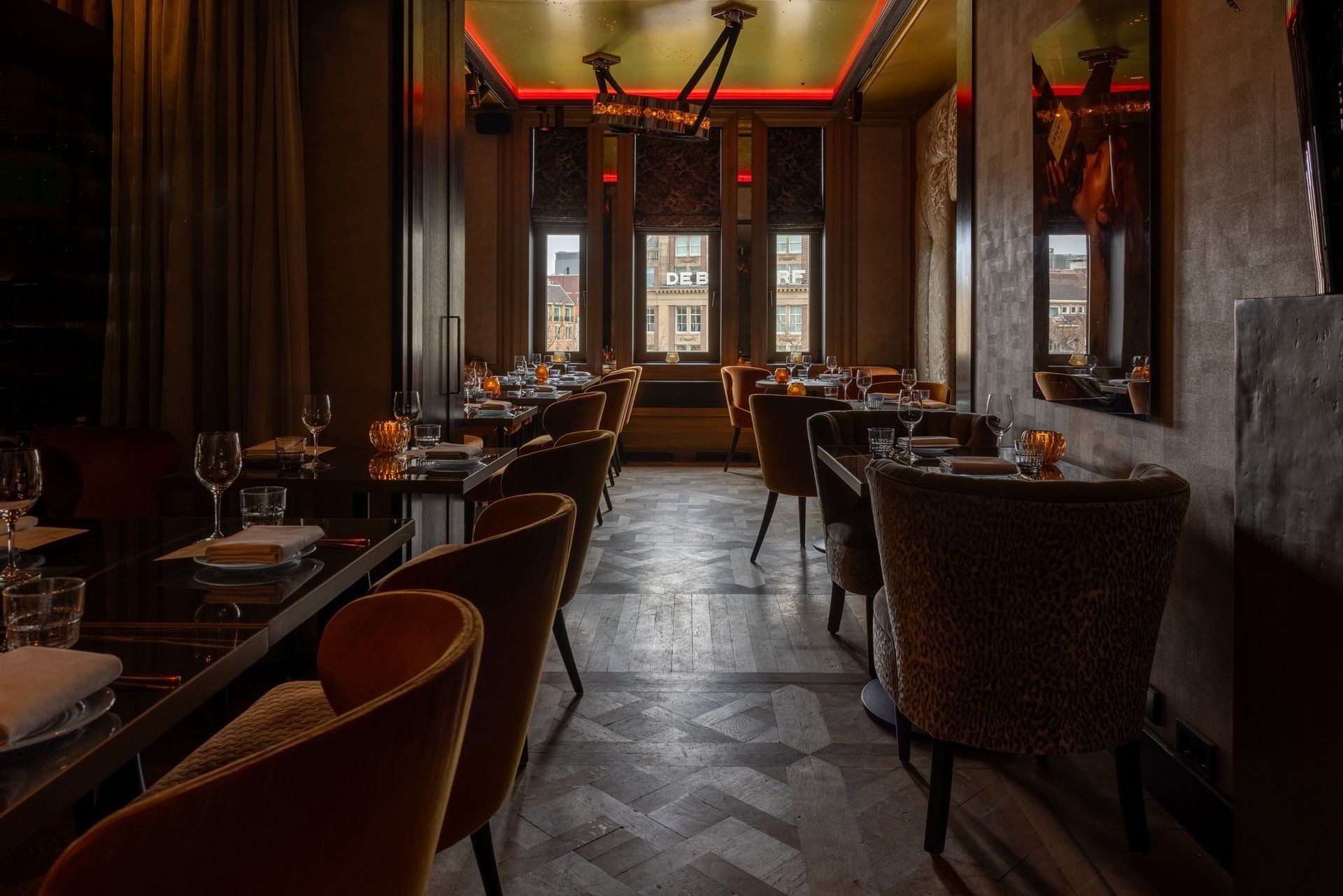 Dimly lit upscale restaurant dining room with set tables, dark walls, and warm red accent lighting.