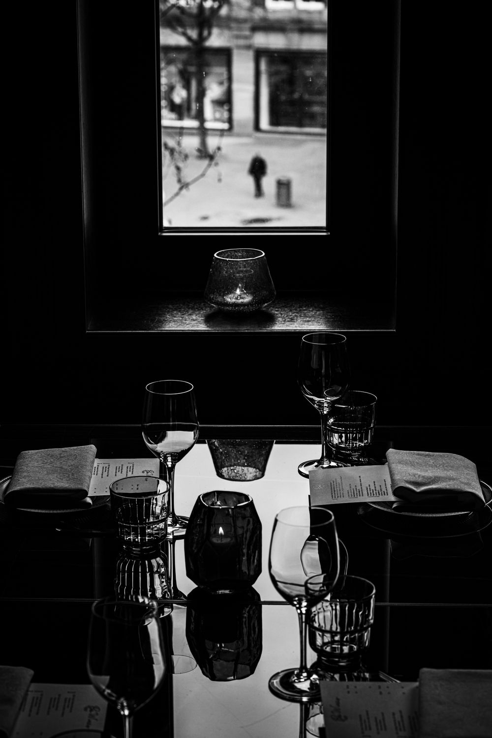 Dim black-and-white café interior with a window view of pedestrians outside.
