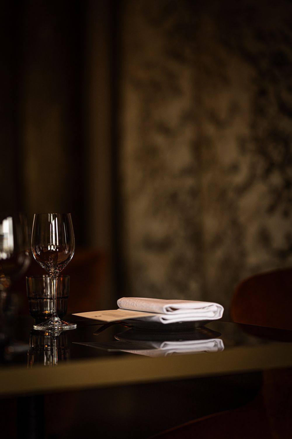 Set dining table with folded napkin, glassware, and reflections in dim warm light