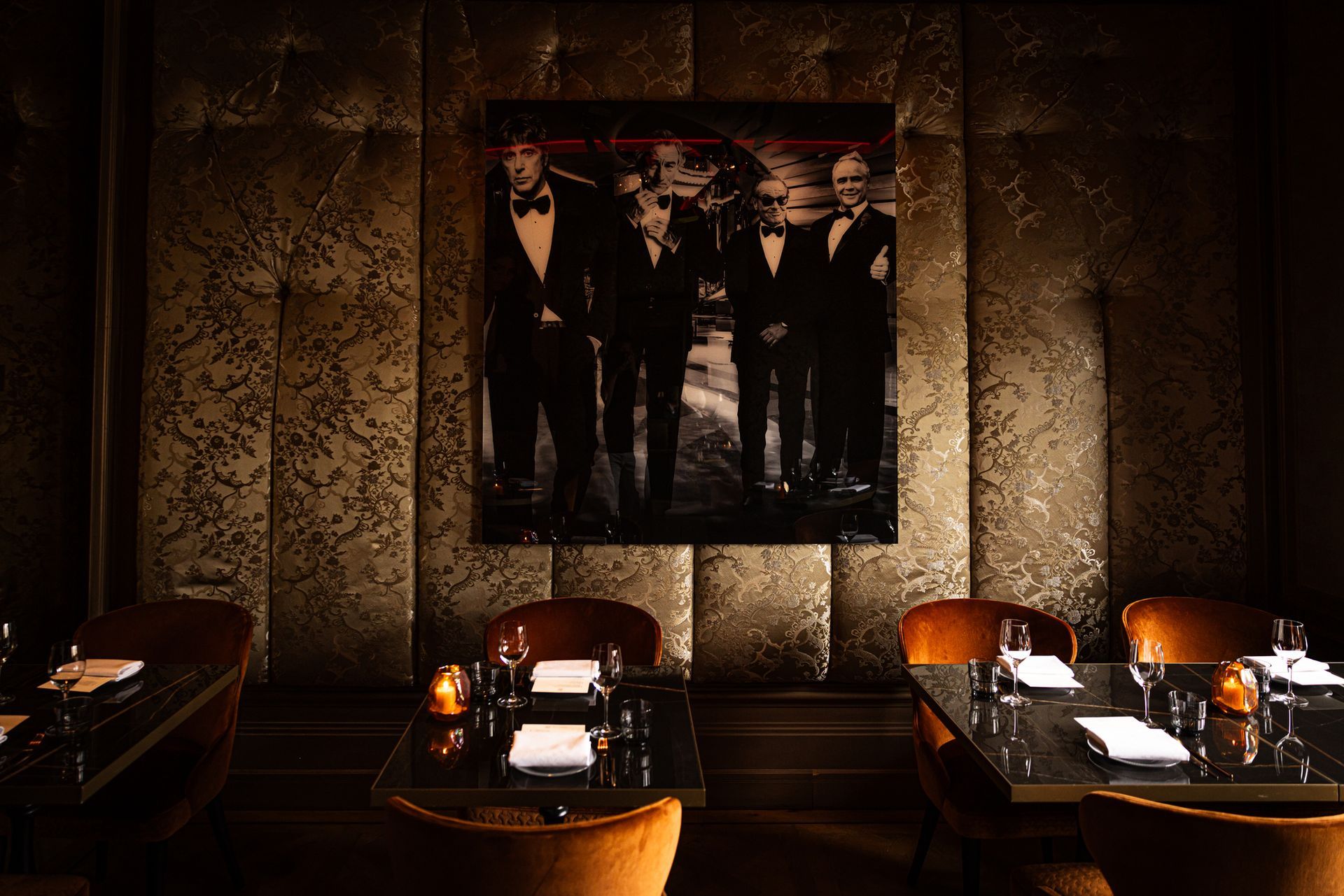 Dim restaurant booth with candlelit tables and a black-and-white wall photo of men in suits