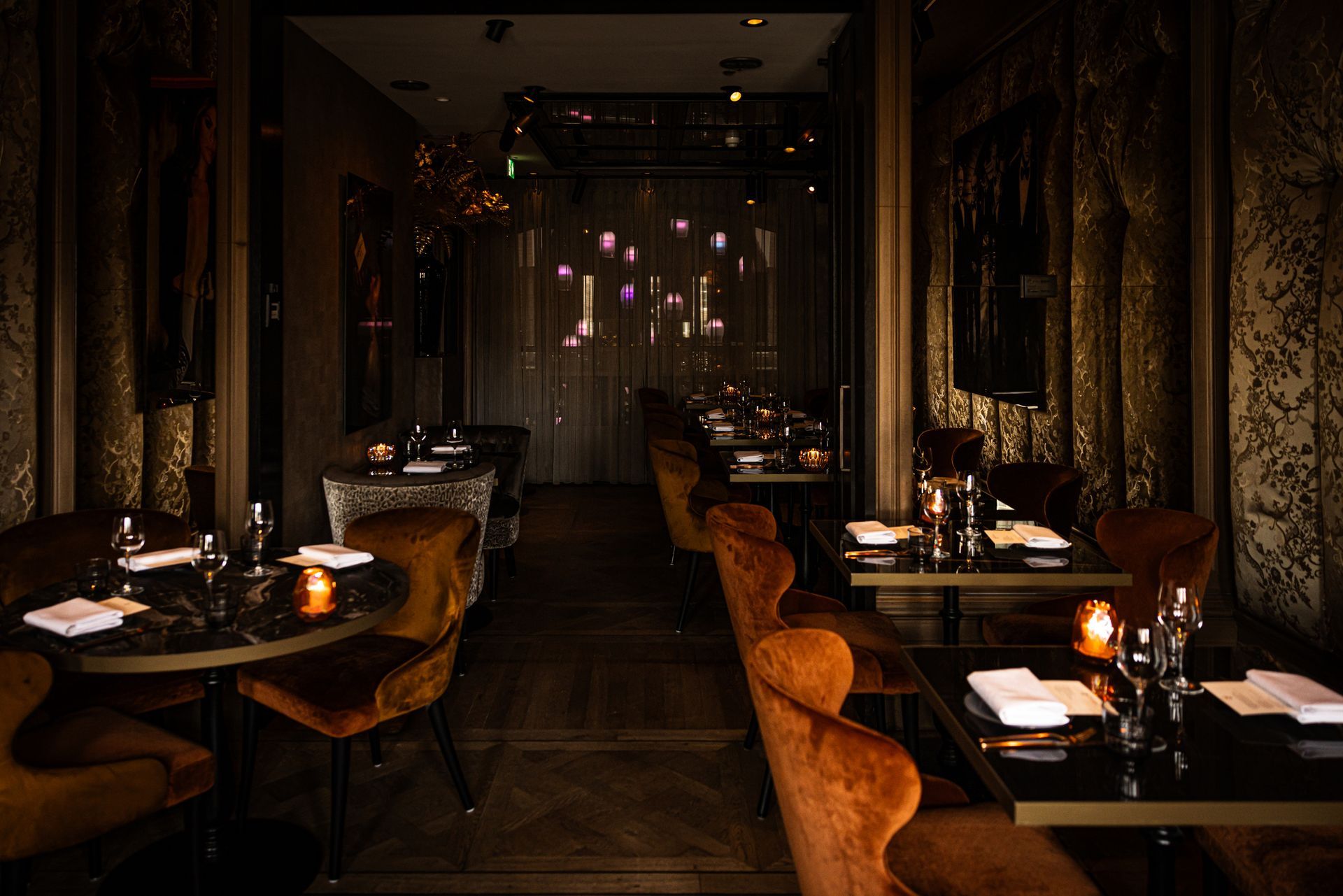 Dimly lit upscale restaurant interior with set tables, orange chairs, and hanging pink lights