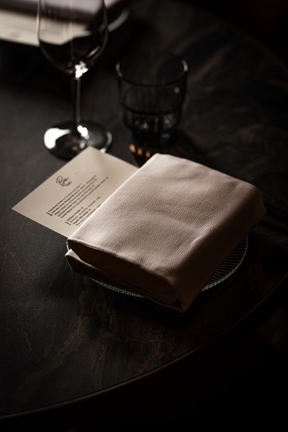 Folded napkin on a dimly lit restaurant table beside a wine glass and menu