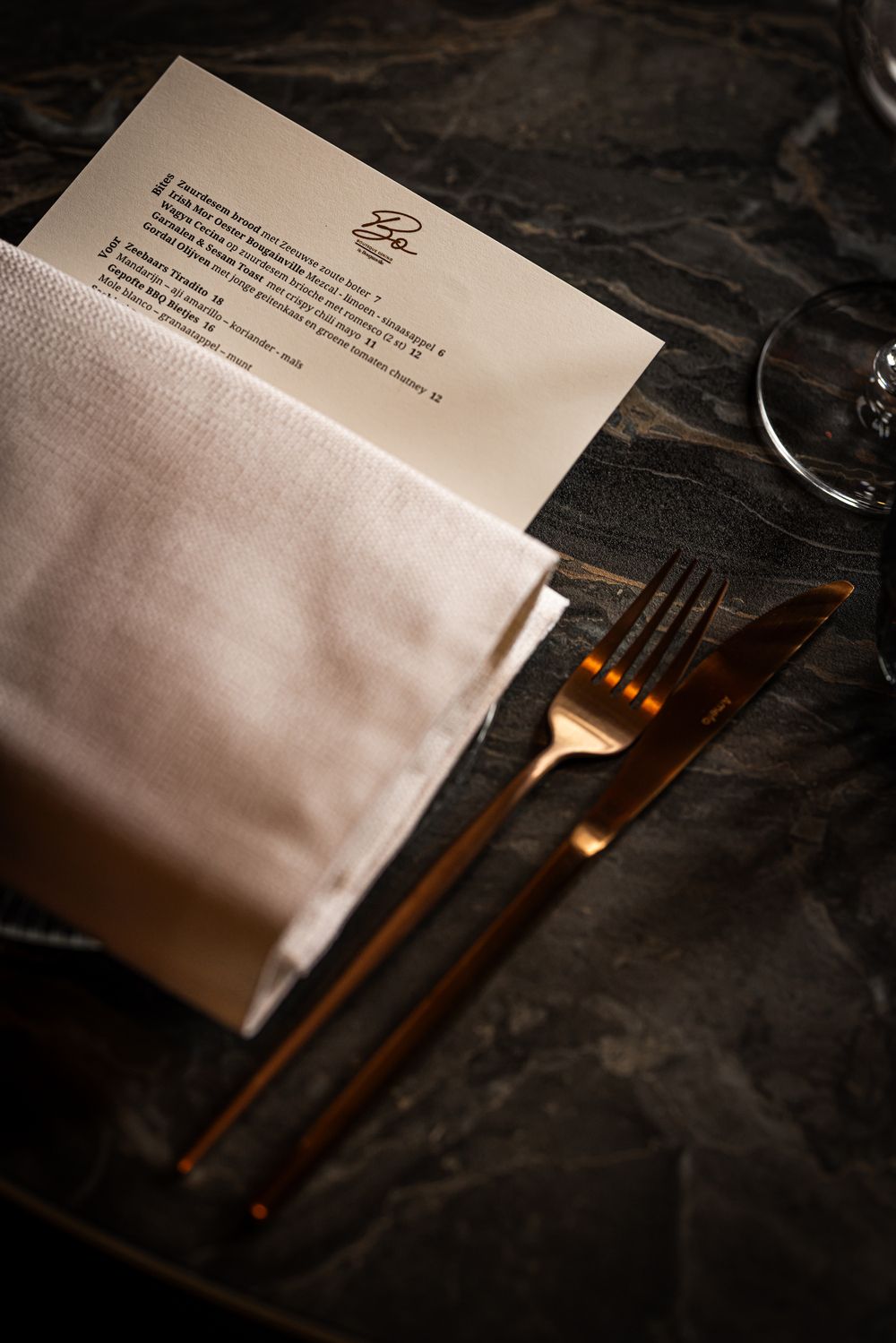 White folded napkin beside a menu on a dark table, with fork, knife, and warm candlelight