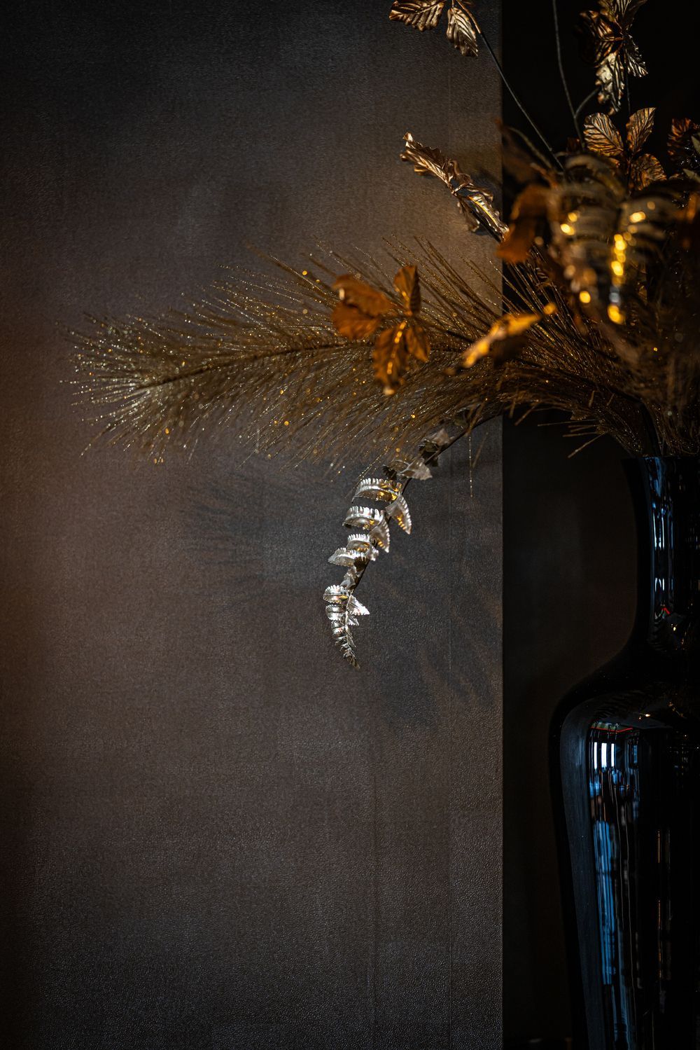 Dark vase with gold dried flowers against a textured gray wall in warm light