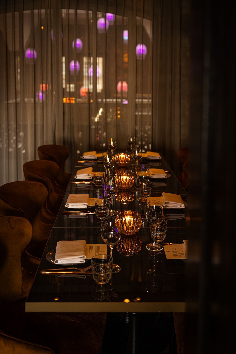 Dimly lit elegant dining table set with candles, glassware, and napkins in a dark restaurant