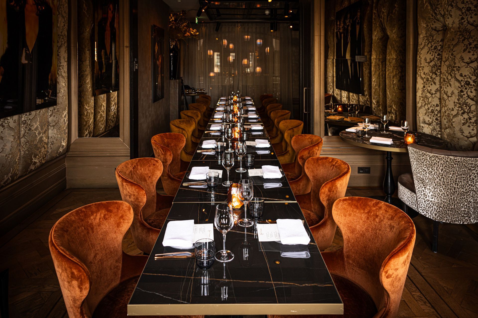 Elegant long restaurant dining table set with orange chairs in a dimly lit hallway-like room