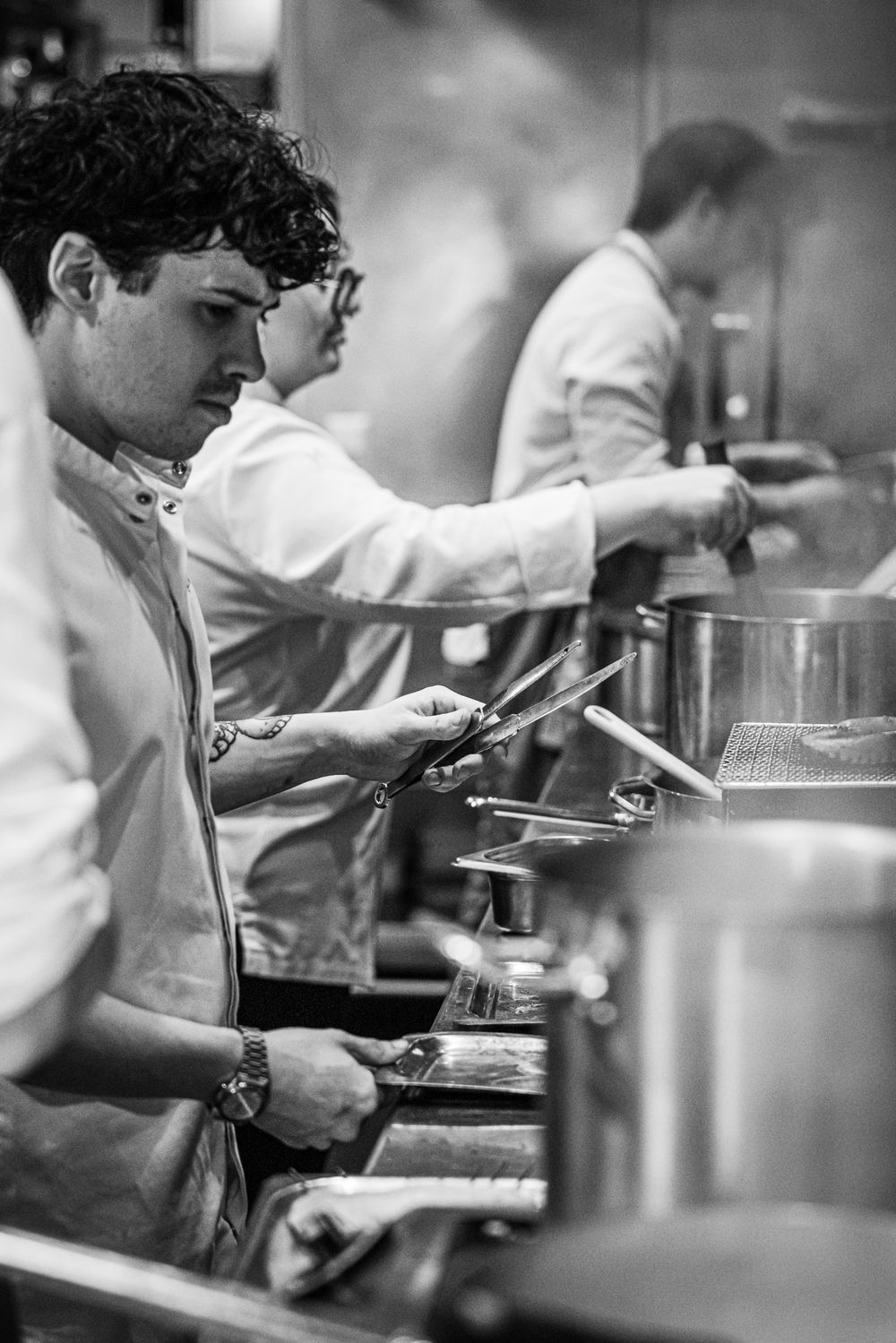 Chef plating food in a busy kitchen, with steam rising from large pots.