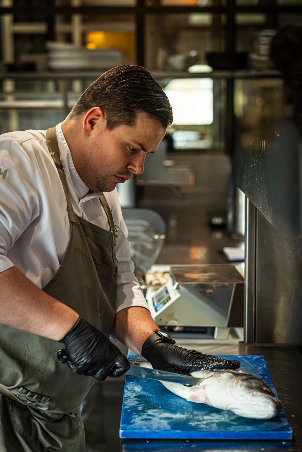 Chef filleting a fish on a blue cutting board in a kitchen