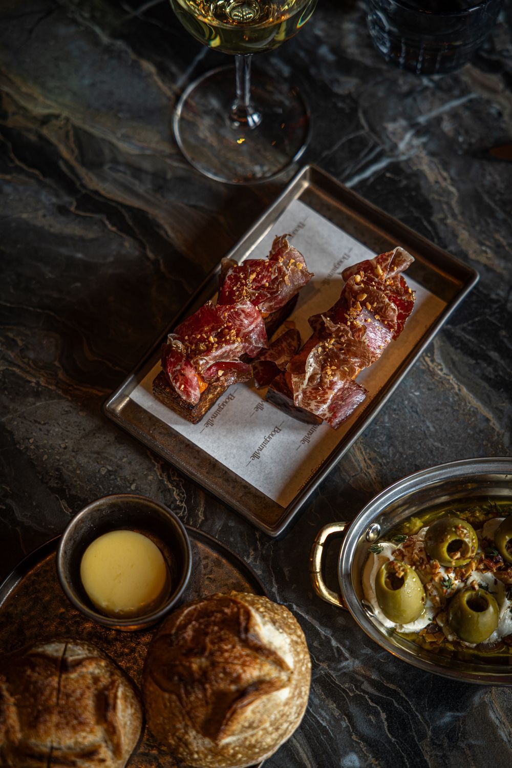 Grilled meat skewers on a tray with bread, sauce, and a drink on a dark table