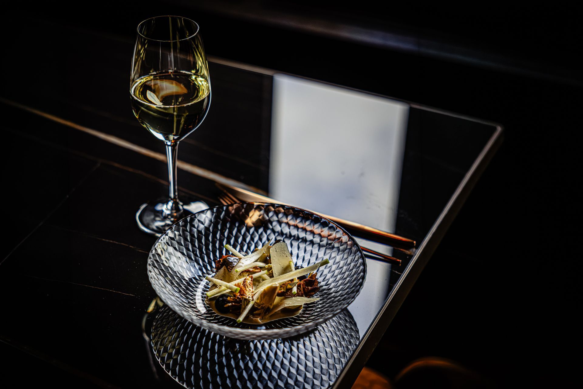 Wine glass and bowl of pasta on a mirrored table in dim lighting