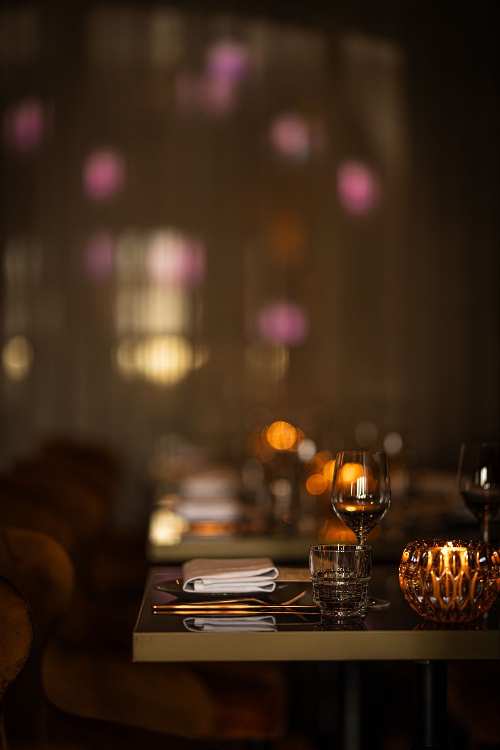 Dimly lit restaurant table set with plates, glasses, and warm candlelight bokeh in the background