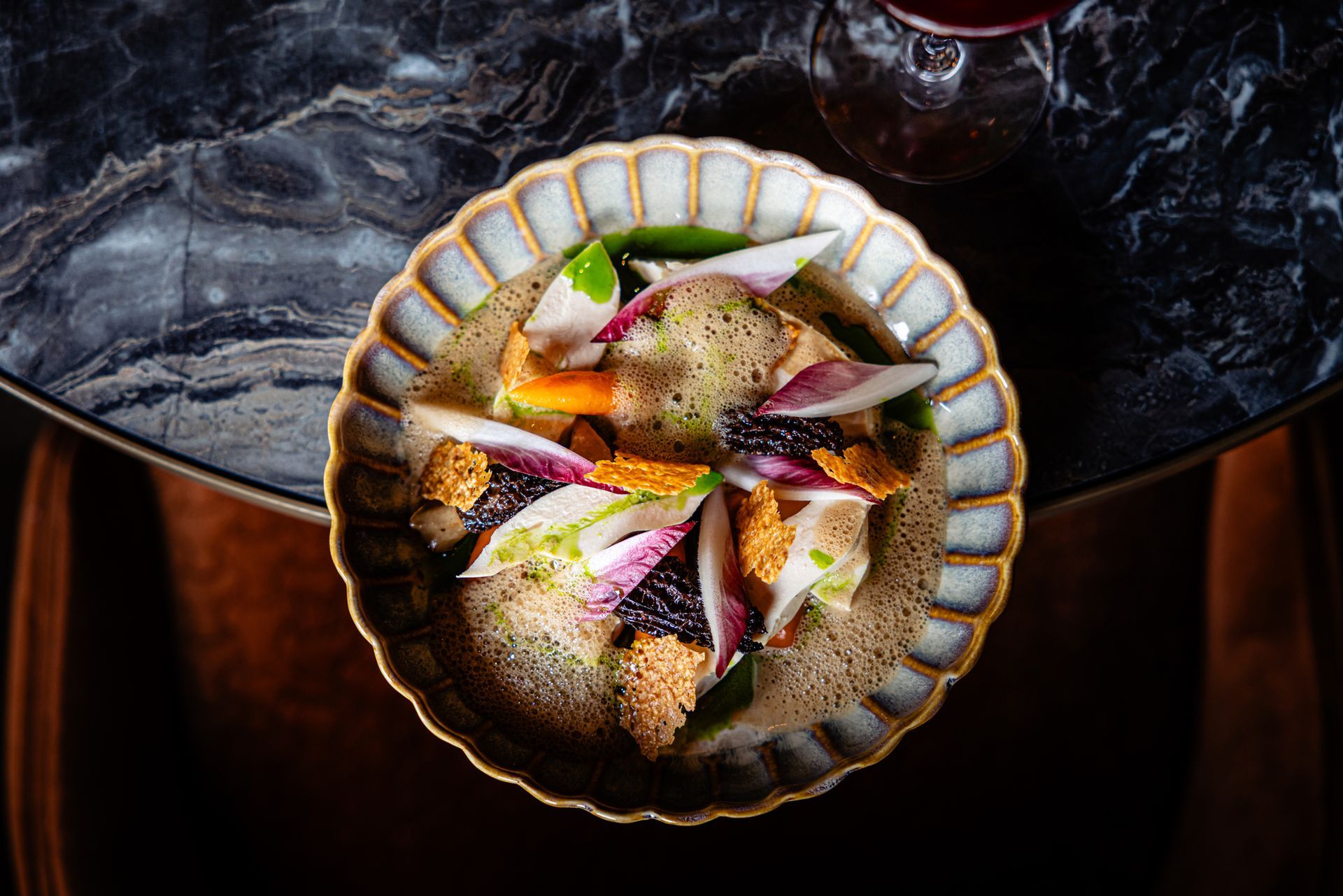 Overhead view of a scalloped bowl of garnished salad on a dark table