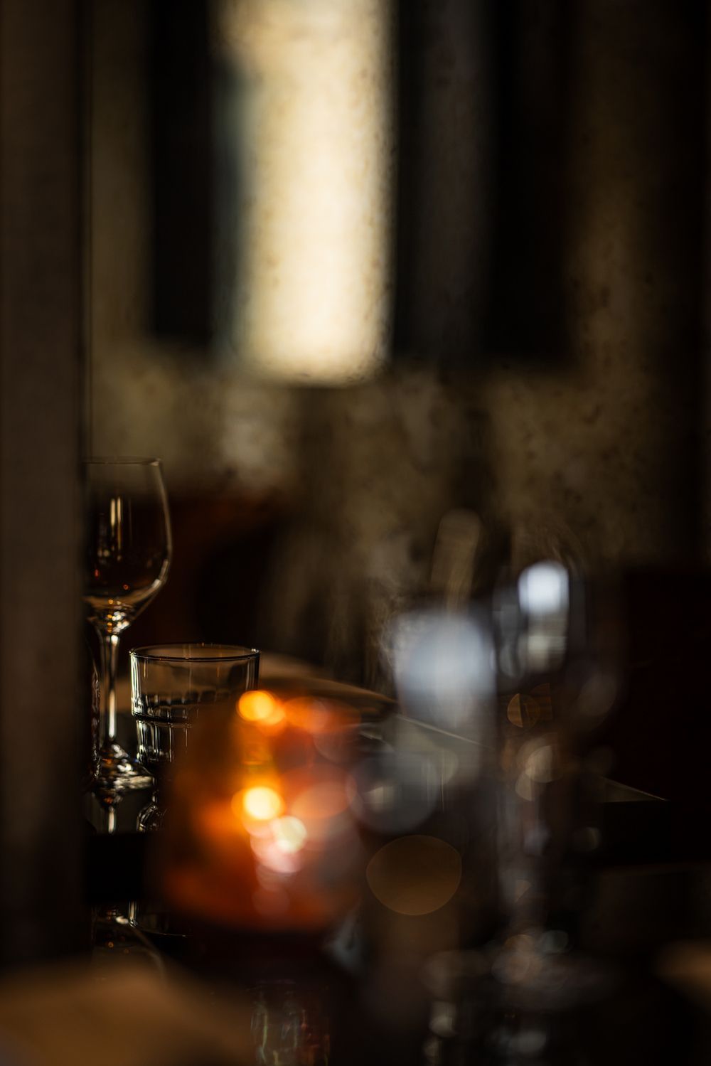 Dim restaurant table with wine glasses and a glowing candle in soft focus.