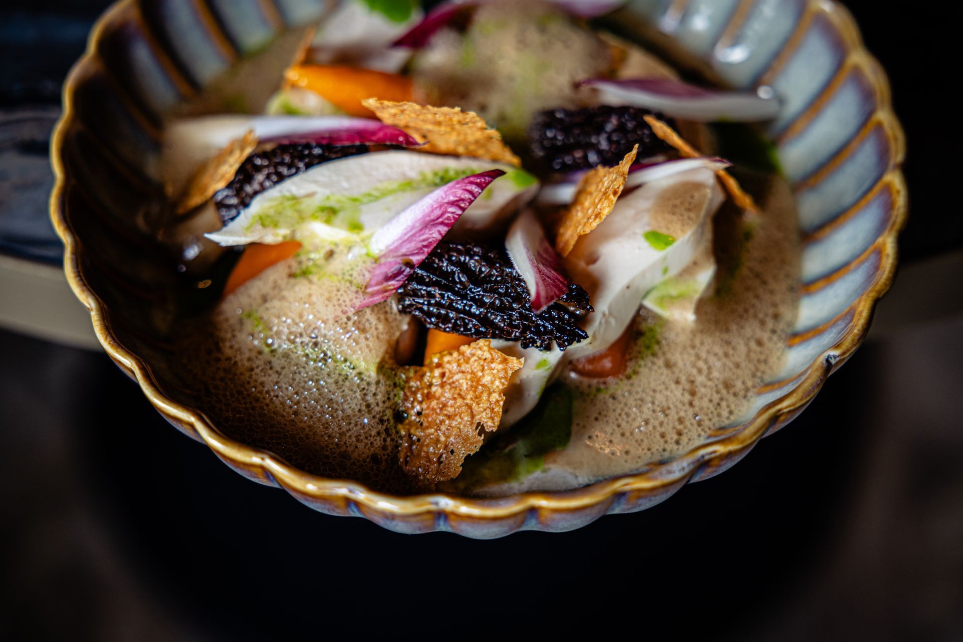 Gourmet plated dish with seared fish, foam sauce, and colorful vegetable garnish in a scalloped bowl